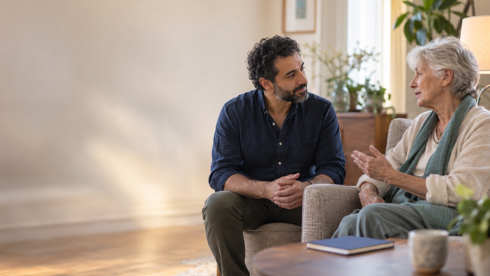 A companion listening to an older adult in a quiet, sunlit room.