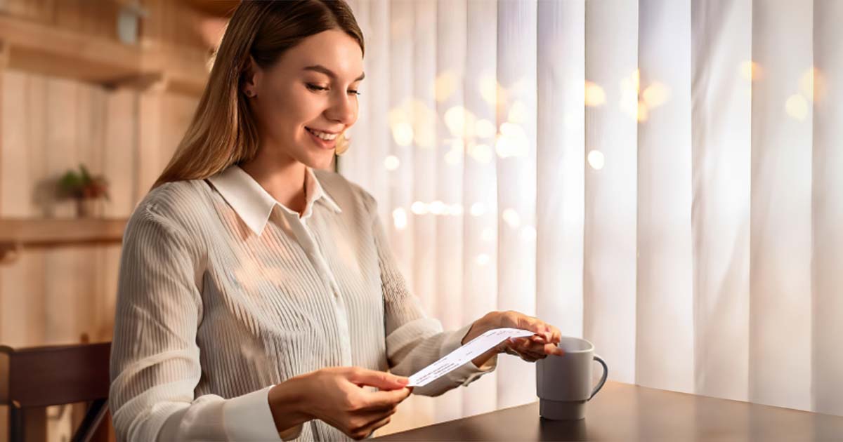 Young woman smiling an looking at her paycheck in her kitchen