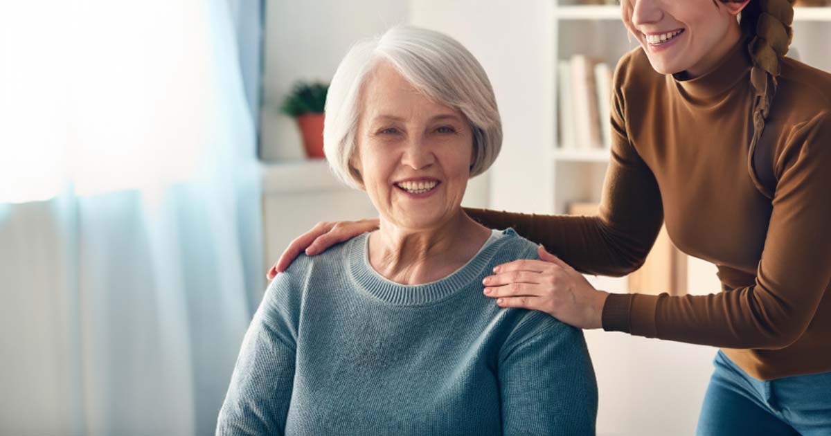 Happy elderly woman sitting with a person touching her shoulders and comforting her