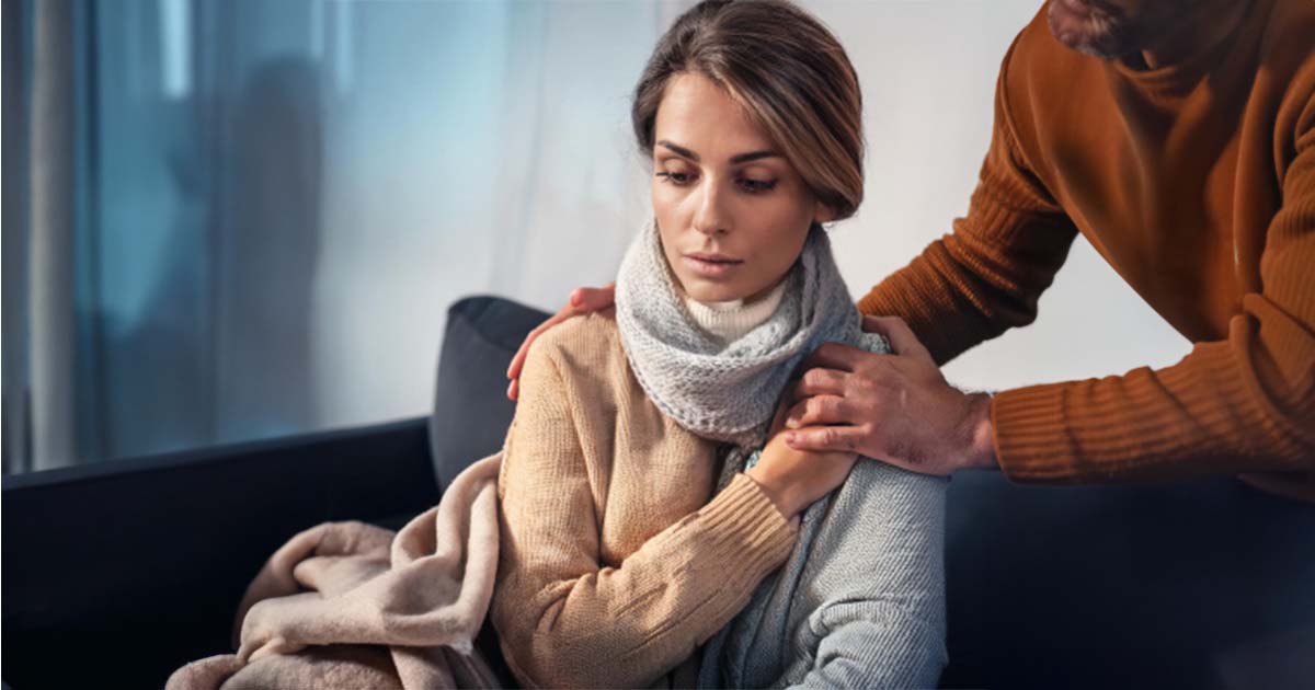 Young female looking concerned and being comforted by a man as he puts his hands on her shoulders to comfort her